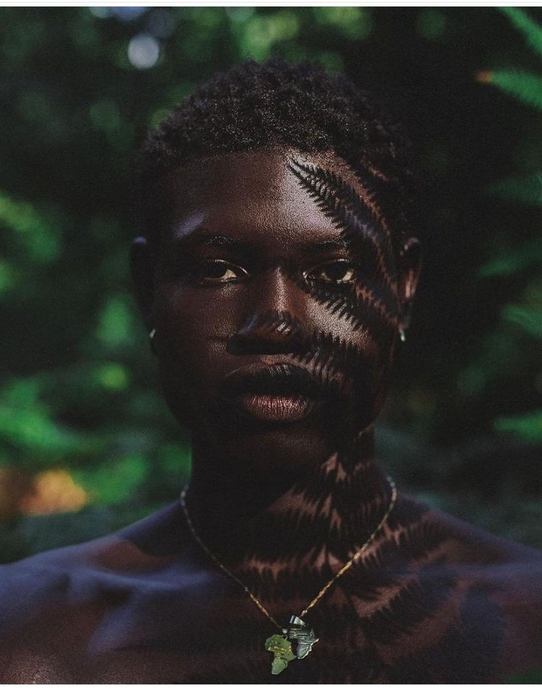 Afro model with frown shadows on their face posed with a African continent necklace