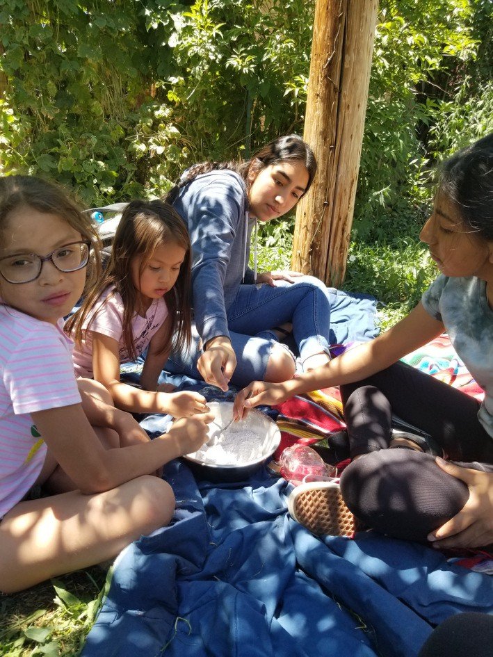 Four Indigenous youth making foot powder on blue blanket under the Trees