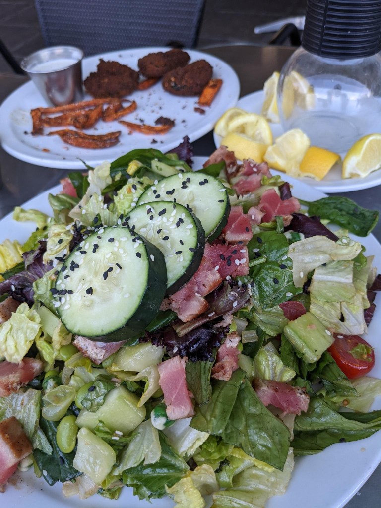 Plates - Tuna Salad topped with cucumbers in the foreground. Sweet potato fries and lemons linger in the background.