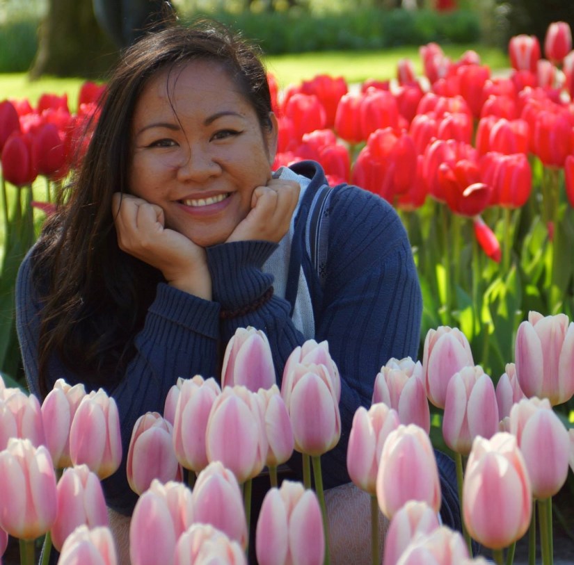 Mayo with closed palms under chin. Smiles among pink Tulips.