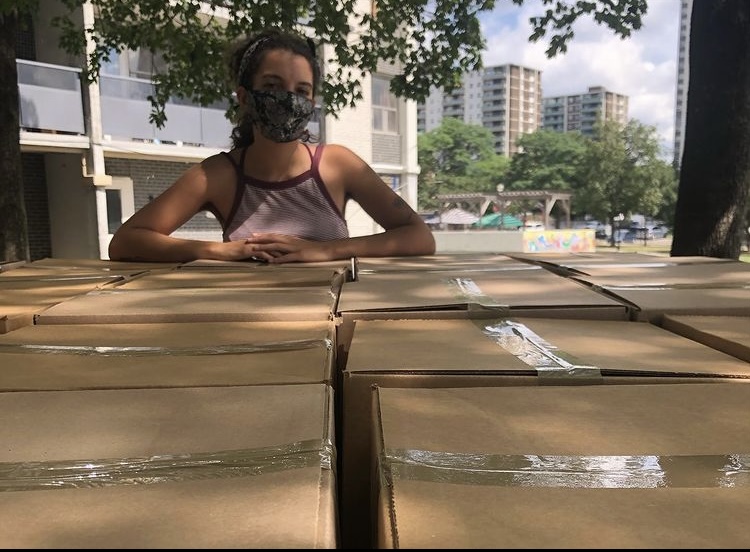 yasmine wears a face mask with arms folded over a stack of boxes.
