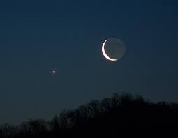 A sliver of the Moon illuminates in the night sky opposite a single Star. The wild land below in shadow.