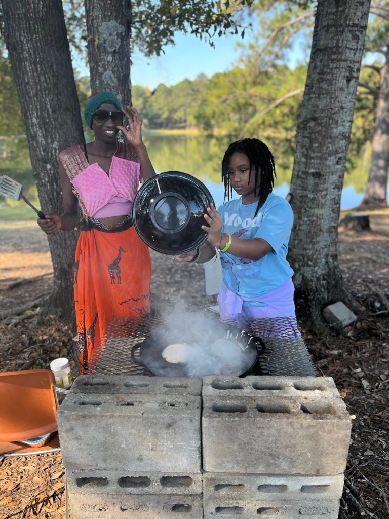Afro Affinity Event. kuwa jasiri (beauty) and Paige (she) make pancakes on open flames. 
